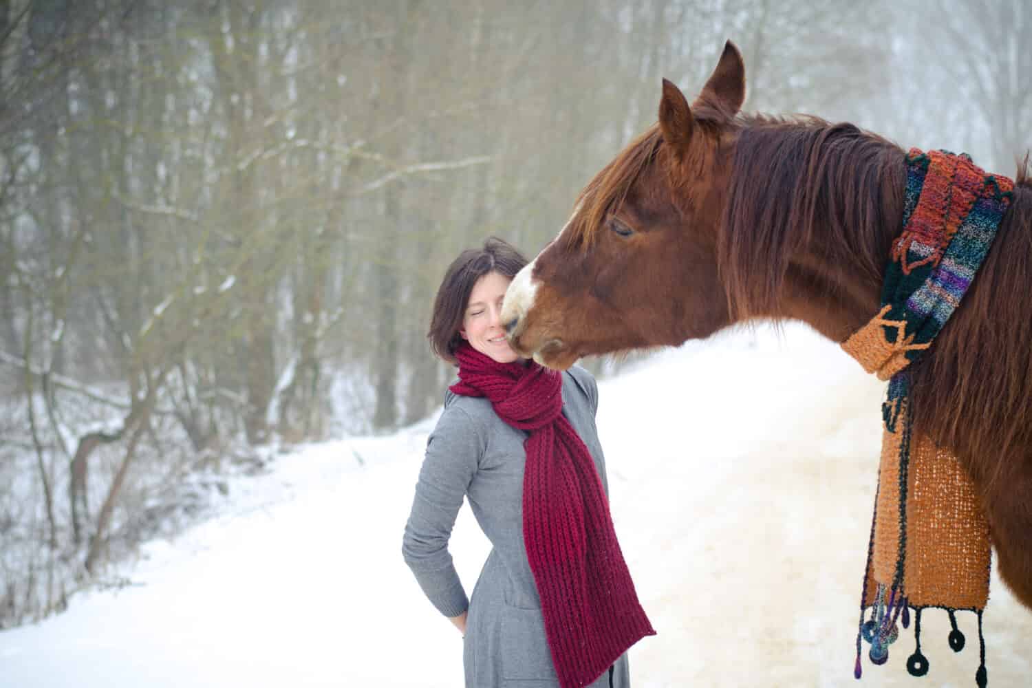 ritratto di ragazza che bacia il cavallo stallone trakehner rosso con sciarpa in inverno