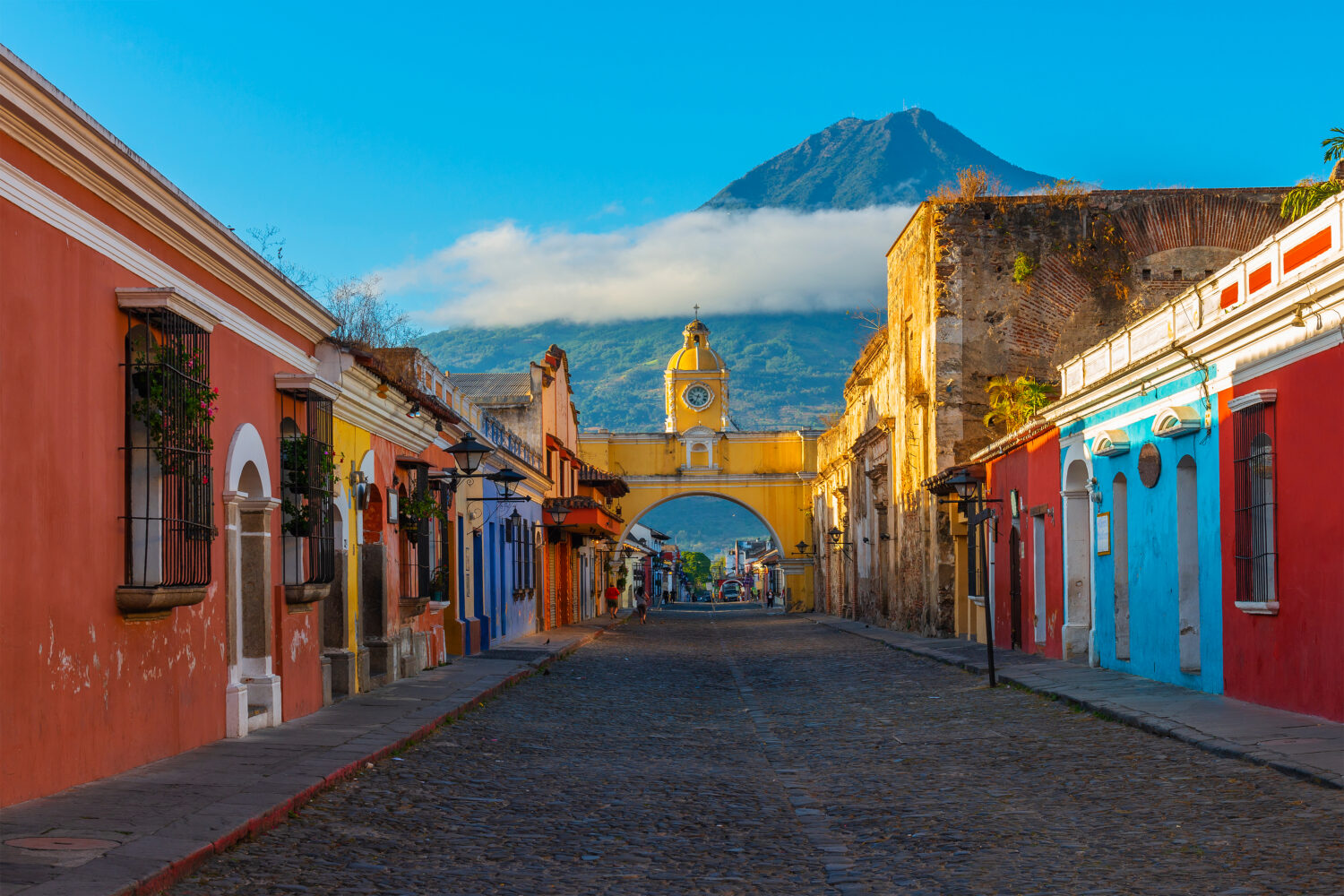 Paesaggio urbano della strada principale e arco giallo di Santa Catalina nel centro storico della città di Antigua all'alba con il vulcano Agua, Guatemala.