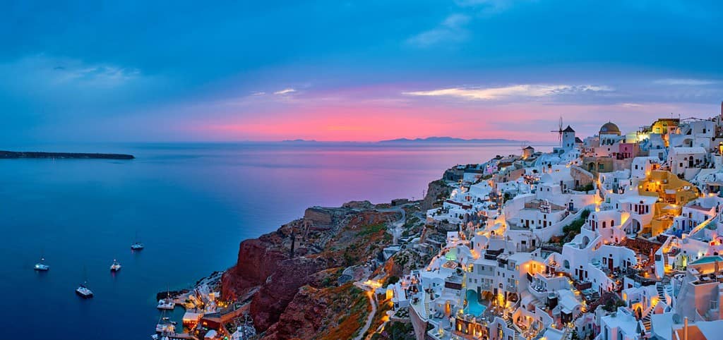 Famosa destinazione turistica iconica greca per selfie, villaggio di Oia con tradizionali case bianche e mulini a vento nell'isola di Santorini nell'ora blu serale, Grecia