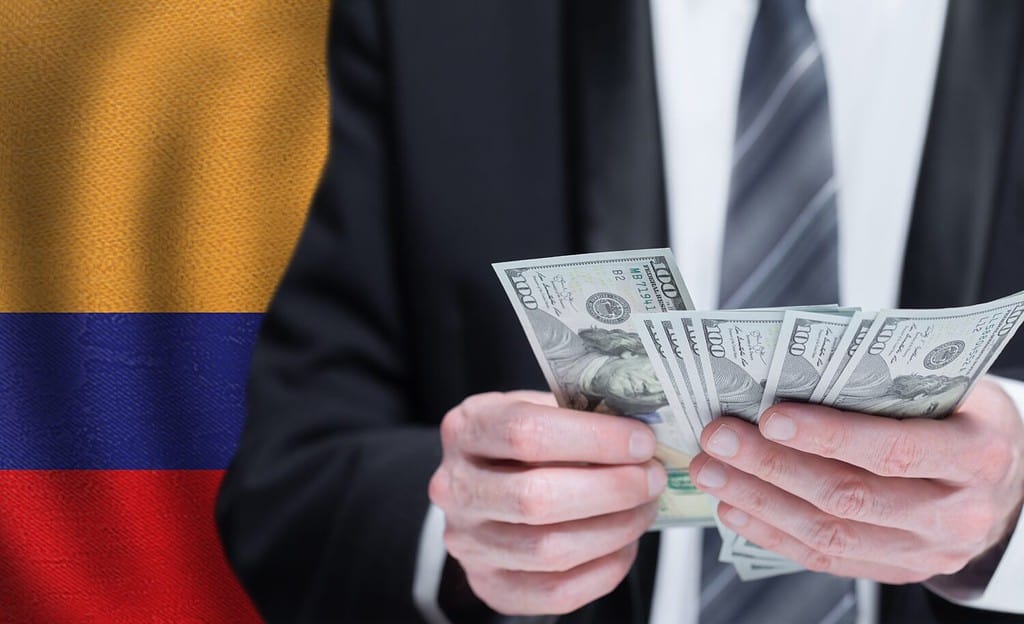 Mani che tengono i soldi del dollaro sulla bandiera della Colombia