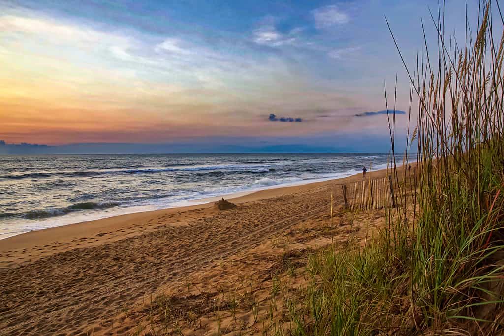 Alba colorata su una spiaggia della Carolina del Nord, onde che si infrangono su una spiaggia sabbiosa incorniciata da dune d'erba.  Anatra, Carolina del Nord