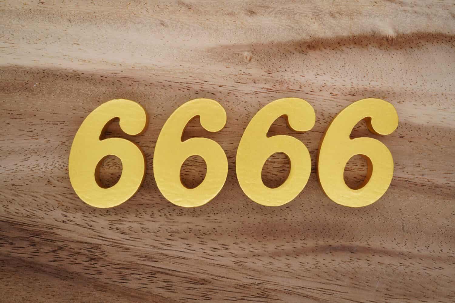 Numeri in legno 6666 dipinti in oro su uno sfondo di tavole fantasia marrone scuro e bianco.
