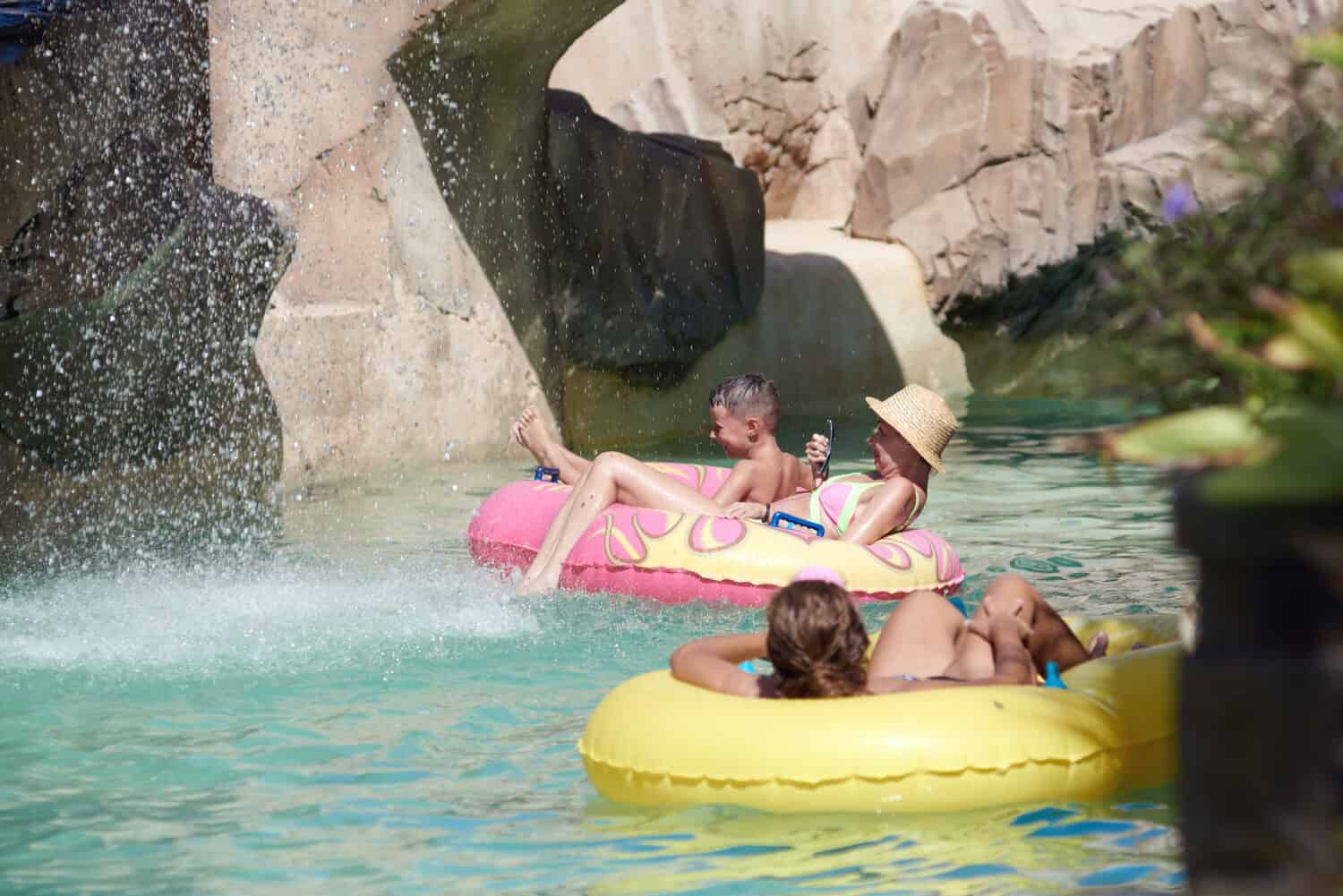 Un simpatico ragazzo europeo e sua madre stanno trascorrendo un periodo fantastico a Waterland.  Stanno nuotando lungo il fiume lento e la finta cascata.  Un sacco di gocce sono ovunque.  Sono in vacanza.