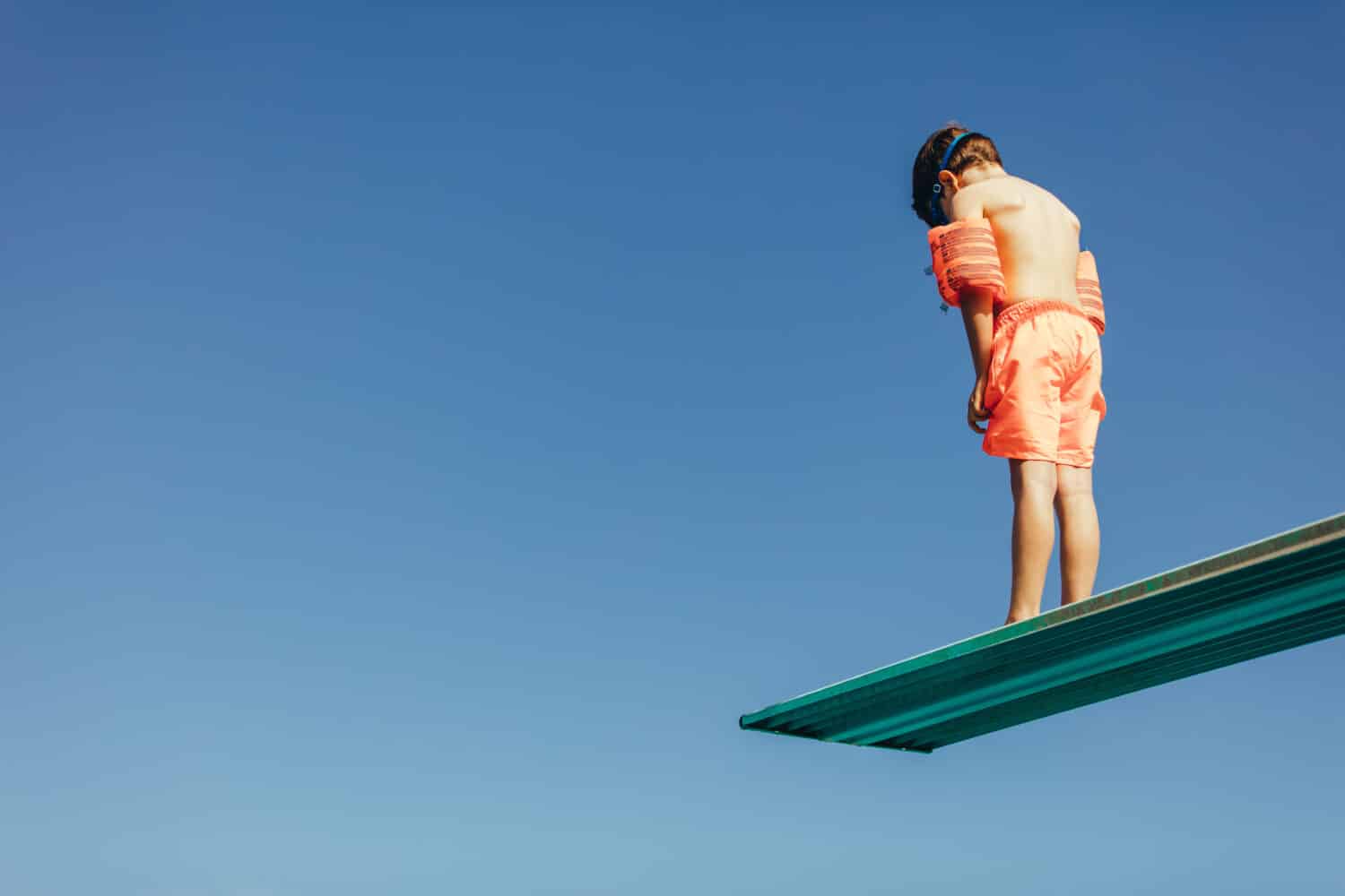 Inquadratura dal basso del ragazzo con le maniche galleggia sul trampolino che si prepara per l'immersione in piscina.  Ragazzo in piedi sul trampolino di immersione contro il cielo.