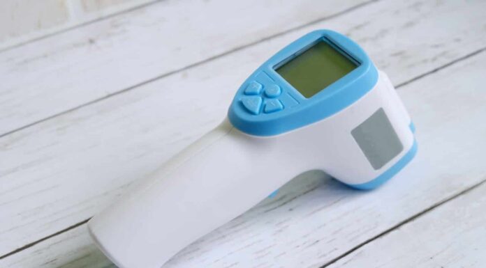 Termometro a infrarossi senza contatto su fondo di legno bianco per misurare la temperatura corporea.  Tema sanitario e medico.