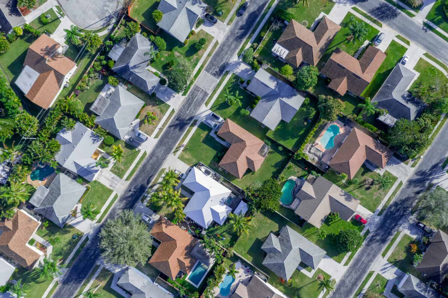 Vista aerea estiva dei tetti caldi e soleggiati della comunità di quartiere con strade diagonali e molte case con piscine e palme. 