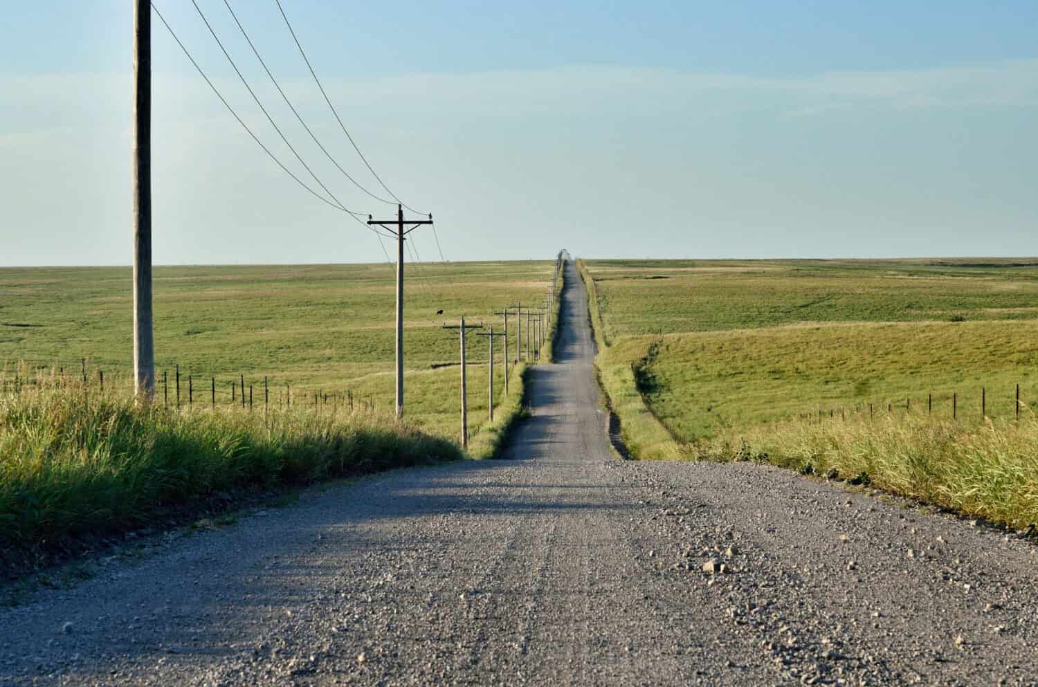 Strada di ghiaia rurale fiancheggiata da pali del telefono che vanno nella prateria aperta in lontananza in Oklahoma