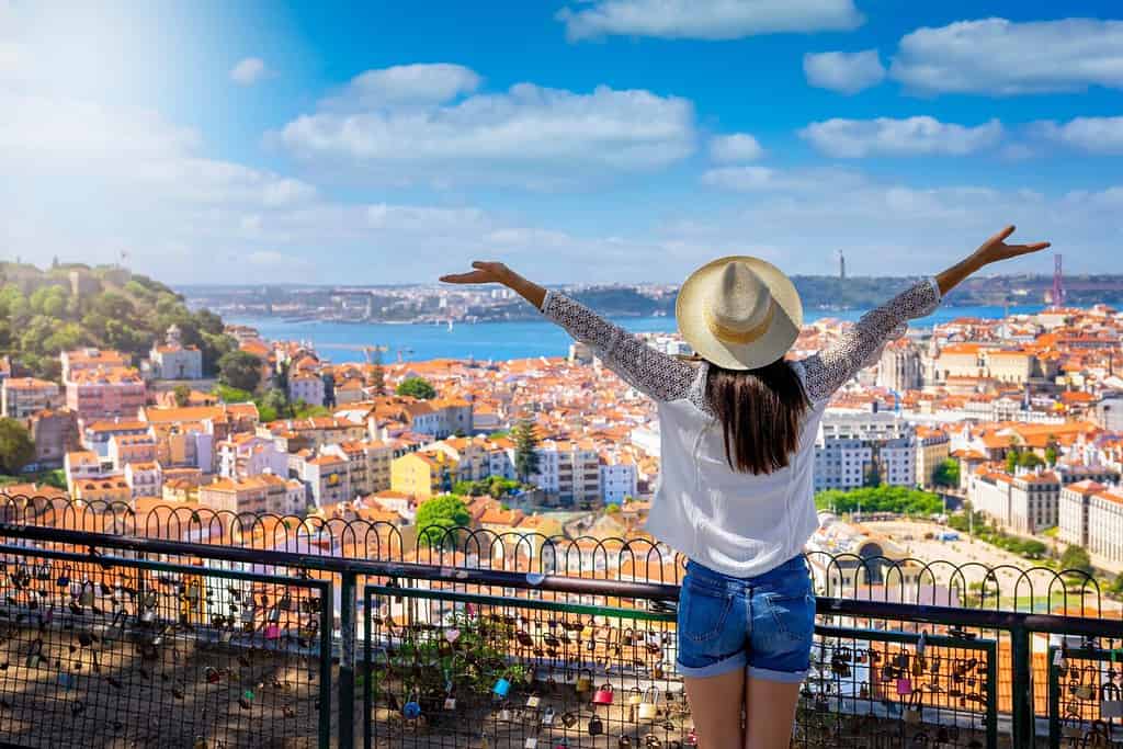 Una felice donna turistica si affaccia sulla colorata città vecchia Alfama della città di Lisbona, in Portogallo, e sul castello Sao Jorge durante il suo viaggio turistico