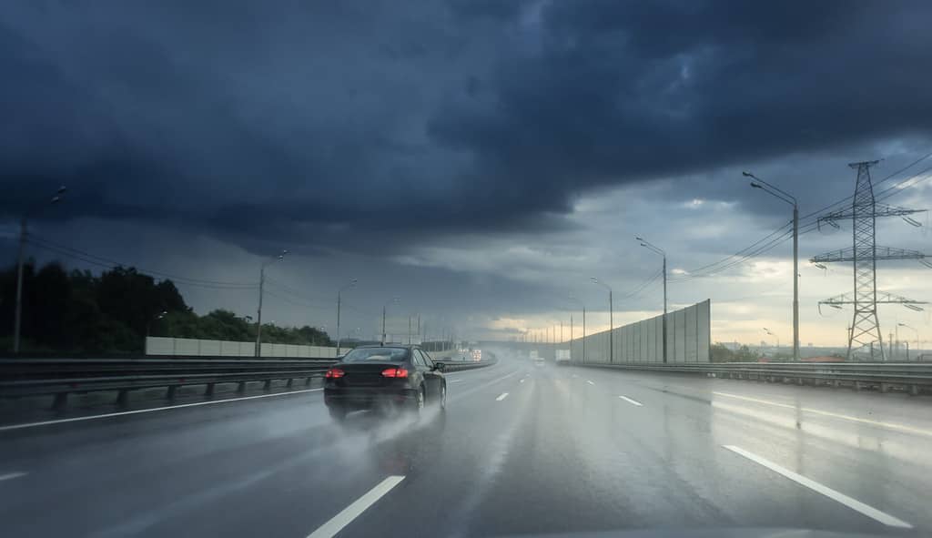 Guidare l'auto sotto la pioggia su strada bagnata asfaltata.  Nuvole e sole.