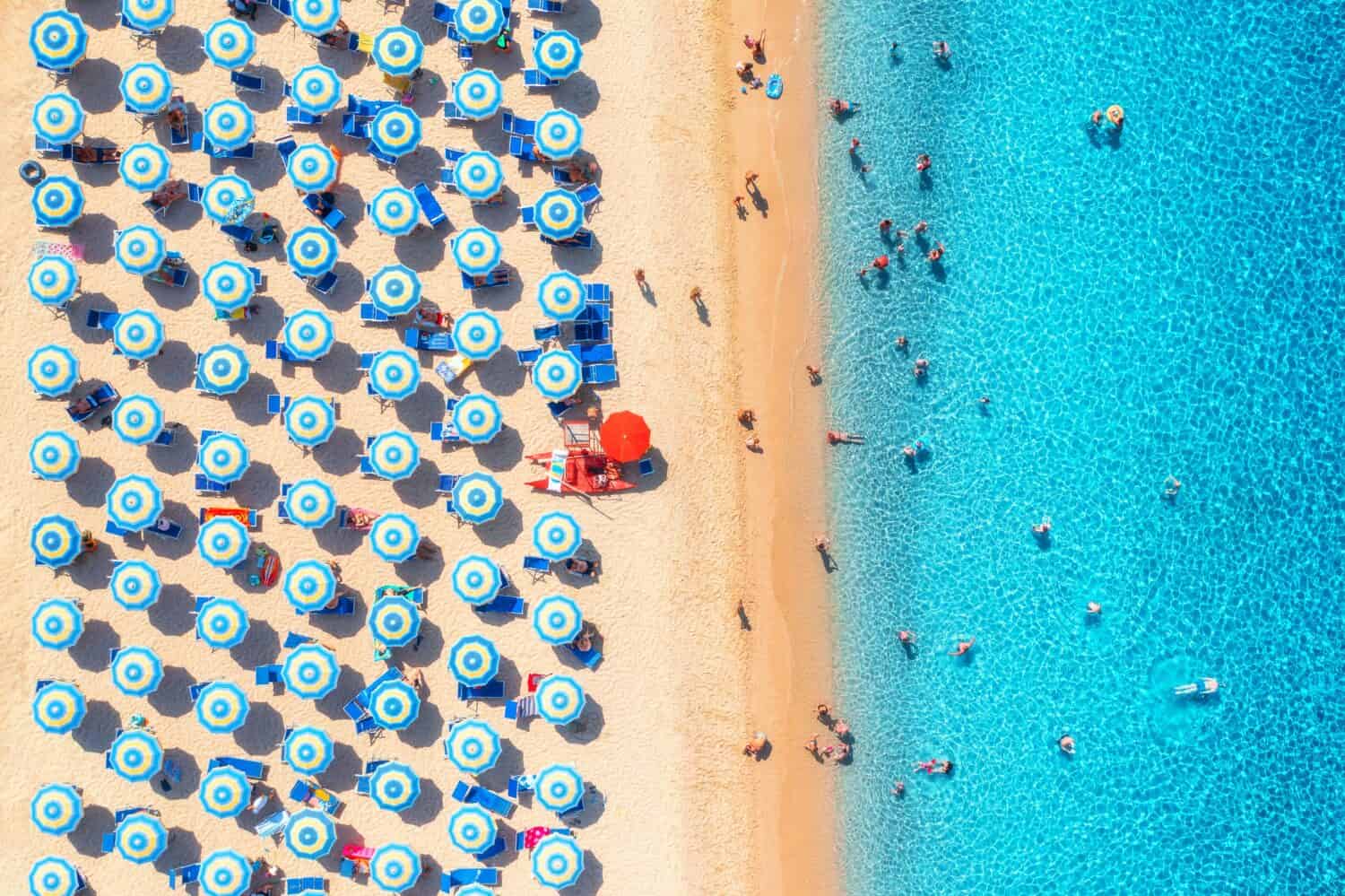 Vista aerea di ombrelloni colorati sulla spiaggia sabbiosa, persone che nuotano nel mare blu durante la giornata di sole estiva.  Resort in Sardegna, Italia.  Vista sul mare tropicale con acqua turchese.  Viaggi e vacanze.  Vista dall'alto