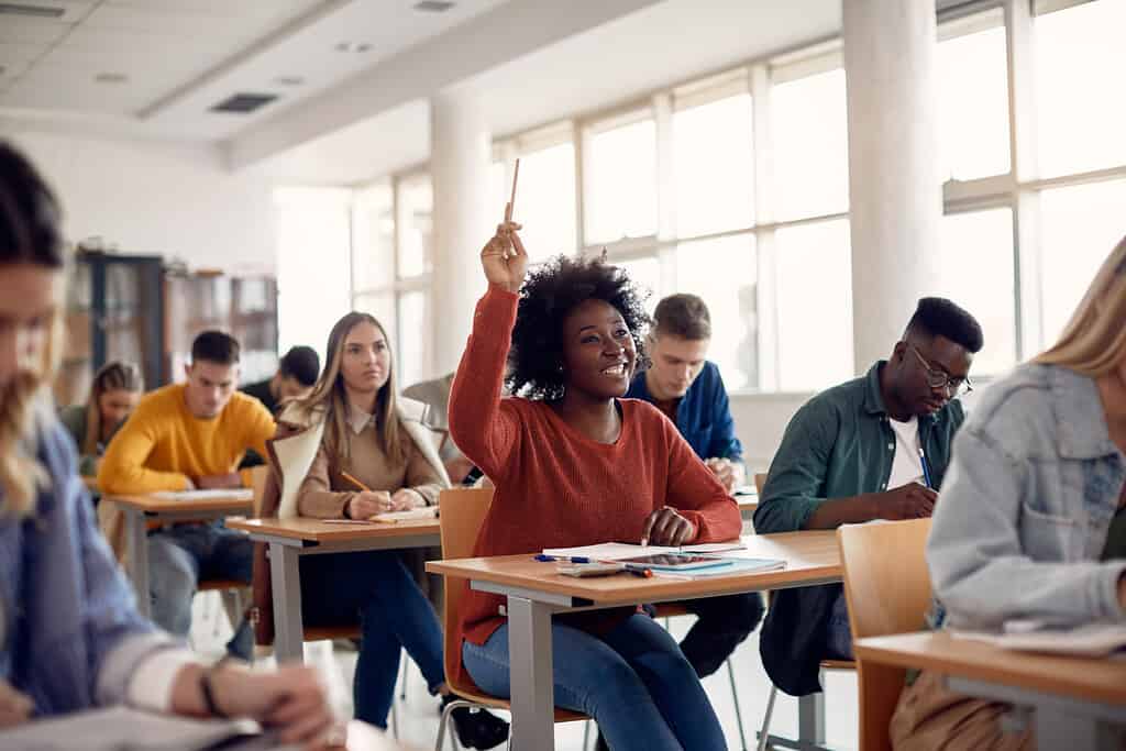 Felice studente afroamericano alzando la mano per fare una domanda durante la lezione in classe.