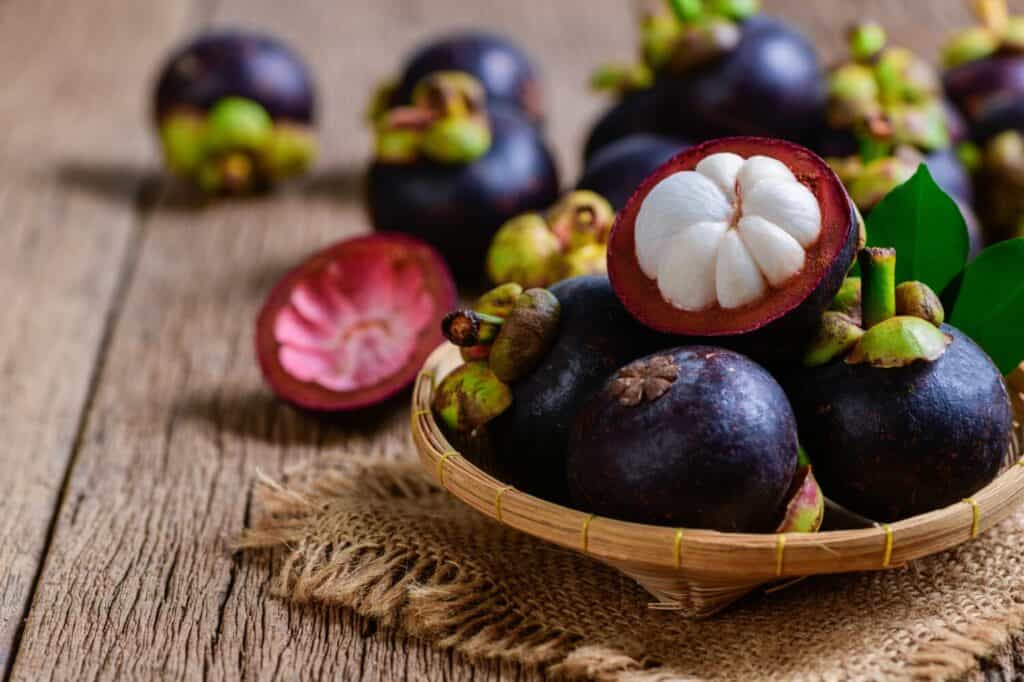 Mangostano fresco in cestino di bambù e su baclground di legno vecchio.  Il mangostano è stato conosciuto come The Queen of Fruits, concetto di frutta asiatica