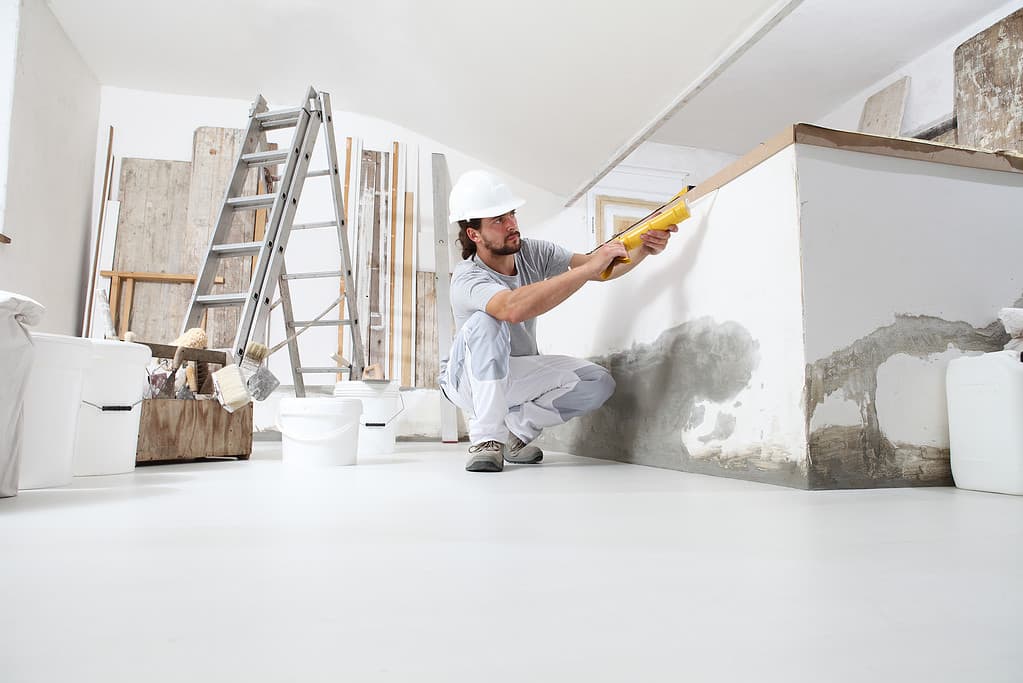 L'uomo stuccatore dell'operaio edile utilizza la pistola per calafataggio nel cantiere di ristrutturazione della casa con strumenti e materiali da costruzione sul pavimento