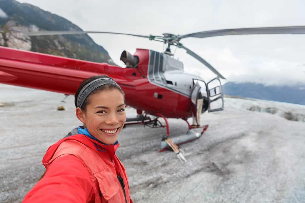 Felice turista che scatta foto di selfie durante l'escursione in elicottero.  Passeggero da crociera asiatico della donna sull'escursione a piedi del ghiacciaio di attività della riva in Alaska, Stati Uniti.