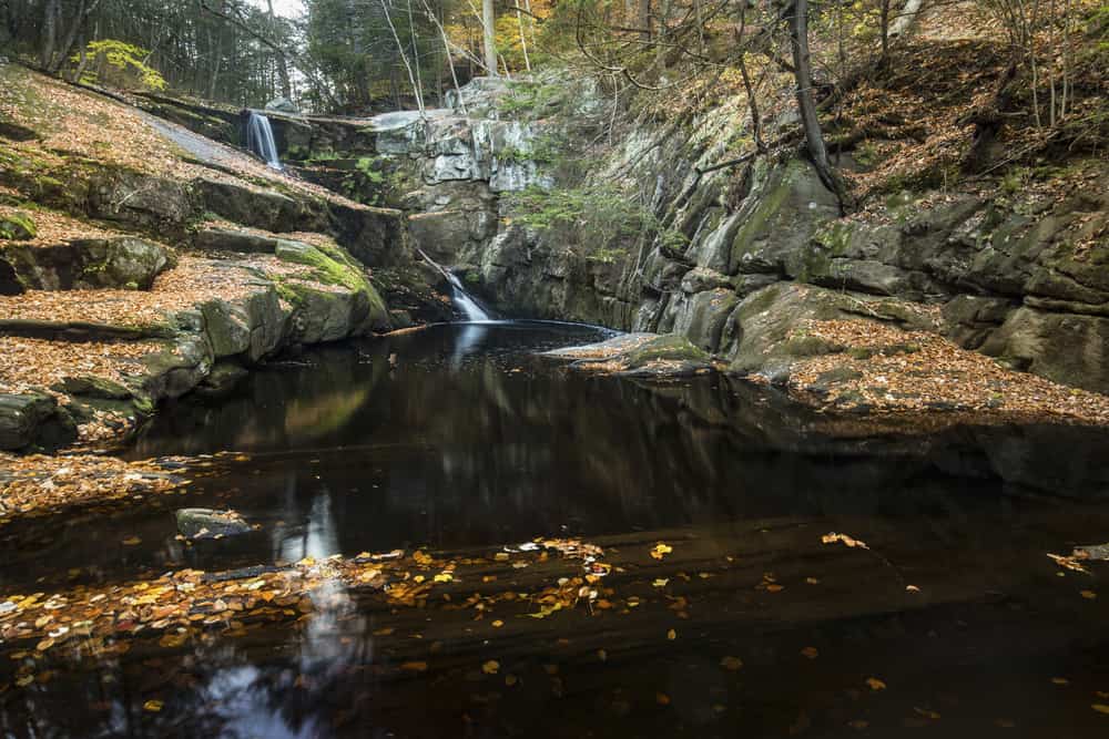 Acqua sfocata e nebbiosa di una cascata all'Enders State Park a Granby, Connecticut, con riflessi delle cascate e delle foglie autunnali nell'acqua scura.