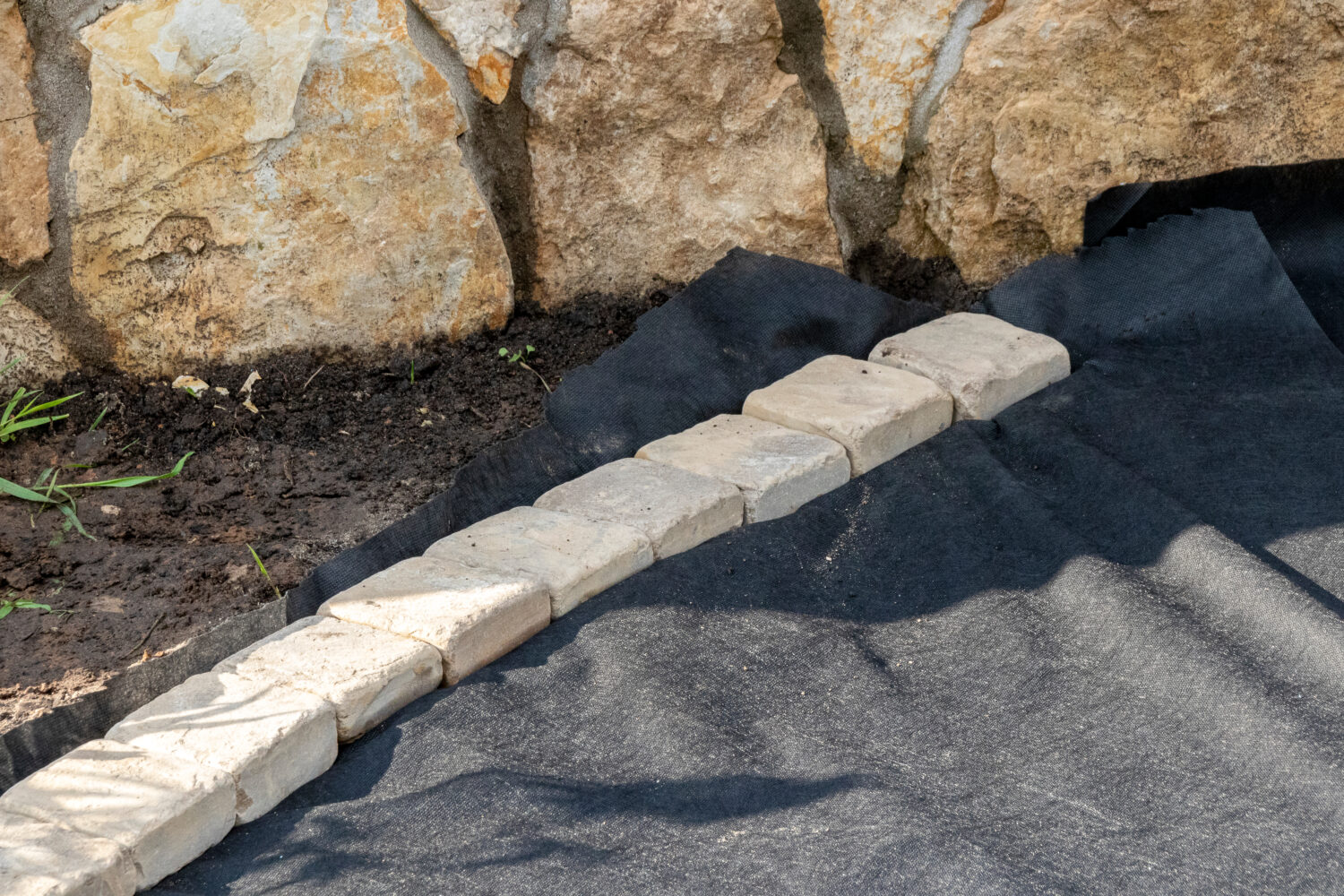 Bordatura di tessuto geotessile posato con pavimentazioni in arenaria nel giardino estivo in fase di ricostruzione
