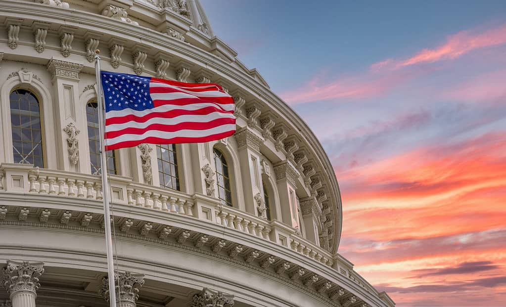 Vista della cupola rotonda del Campidoglio degli Stati Uniti a Washington DC con la bandiera americana stellata sullo sfondo colorato e drammatico del cielo al tramonto
