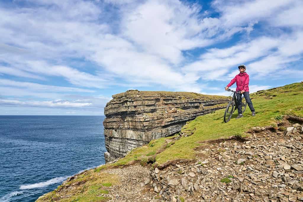 bella donna anziana in mountain bike, in bicicletta sulle scogliere di Dunmore Head vicino a Kilballyowen , nella contea di Limerick nella parte sud-occidentale della Republik d'Irlanda