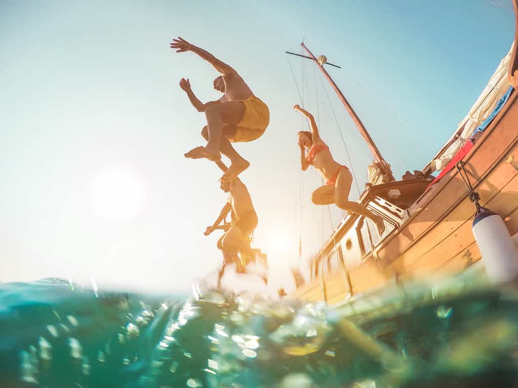 Amici felici che si tuffano in mare dalla barca a vela - Giovani che saltano nell'oceano durante un'escursione estiva - Concetto di vacanza, gioventù e divertimento - Focus principale sull'uomo in primo piano - Distorsione della lente fisheye
