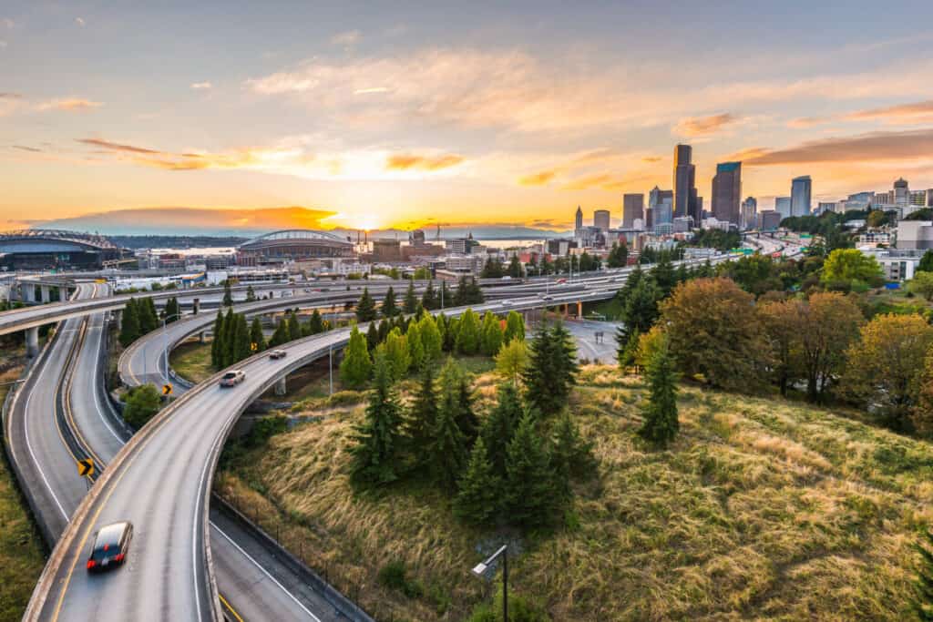 Gli skyline di Seattle e le autostrade interstatali convergono con Elliott Bay e lo sfondo del lungomare al tramonto, Seattle, Washington state, USA.