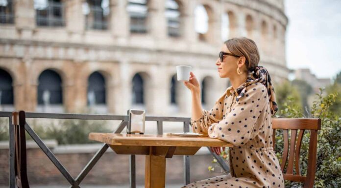 Donna che beve caffè al caffè all'aperto vicino al Colosseo, il punto di riferimento più famoso di Roma.  Concetto di stile di vita italiano e viaggio in Italia.  Donna caucasica che indossa abito e scialle nei capelli