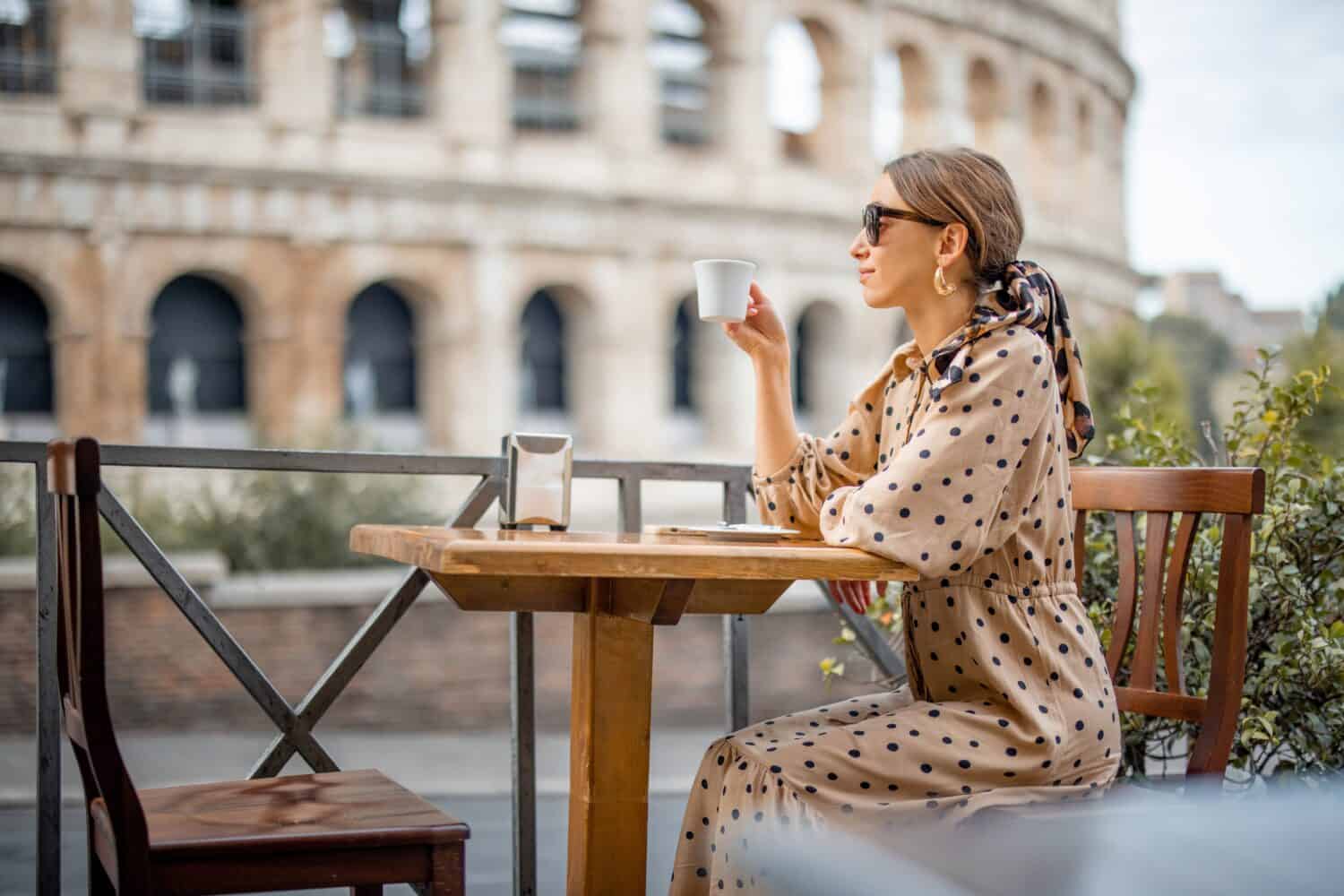 Donna che beve caffè al caffè all'aperto vicino al Colosseo, il punto di riferimento più famoso di Roma.  Concetto di stile di vita italiano e viaggio in Italia.  Donna caucasica che indossa abito e scialle nei capelli