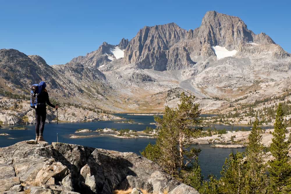 Una donna escursionista si erge in alto sopra il lago Garnett nella Sierra Nevada.  Il deserto di Ansel Adams, Sierra Nevada, California