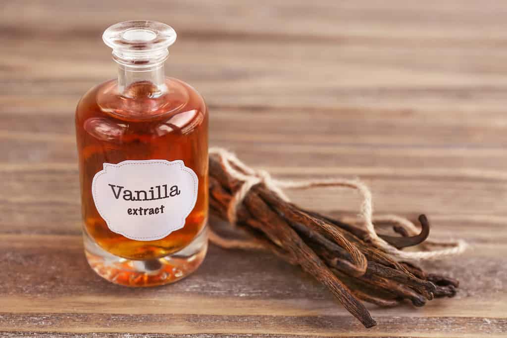 Bottiglia con estratto aromatico e baccelli di vaniglia secchi sul tavolo