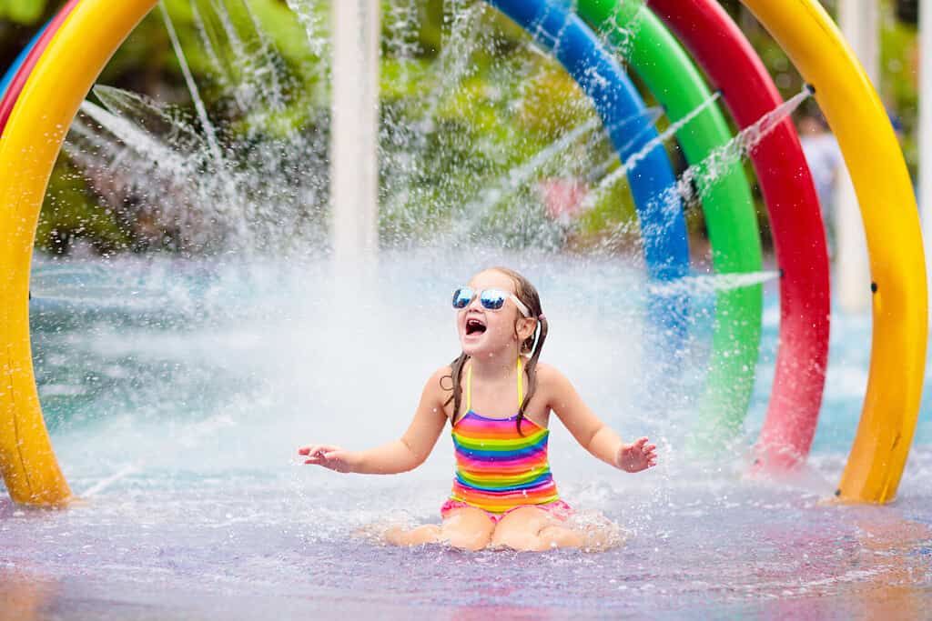 I bambini giocano nel parco acquatico.  Bambini al parco giochi acquatico del parco divertimenti tropicale.  Bambina in piscina.  Bambino che gioca allo scivolo d'acqua durante le vacanze estive in Asia.  Costume da bagno per bambini.