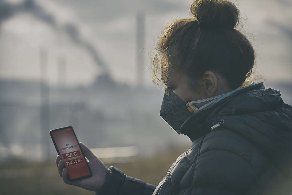 Donna che indossa una vera maschera anti-smog e controlla l'attuale inquinamento atmosferico con l'app per smartphone