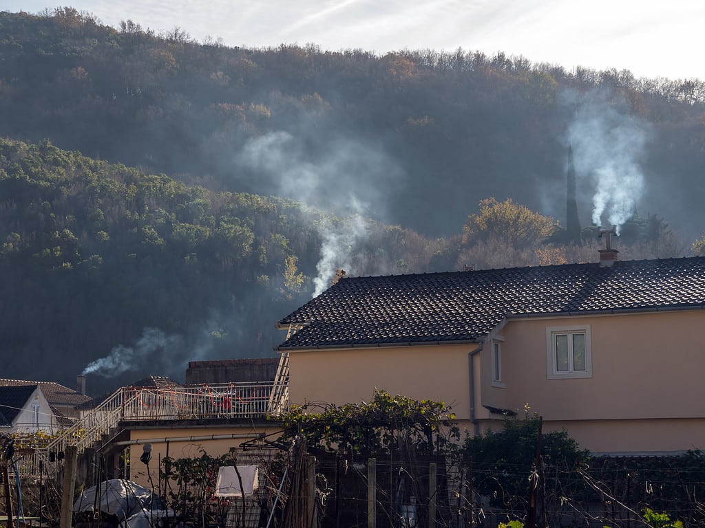 Fumo dai camini delle case di una piccola città con tetti di tegole e alberi verdi in collina sullo sfondo vista laterale