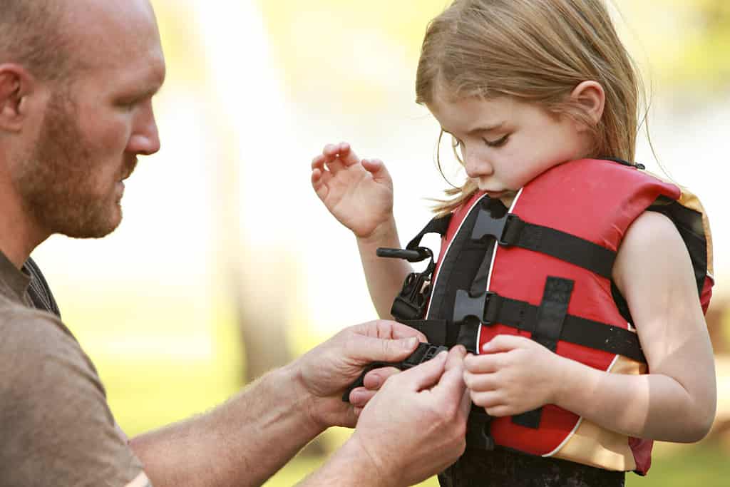 Un padre aiuta la figlia con il giubbotto di salvataggio