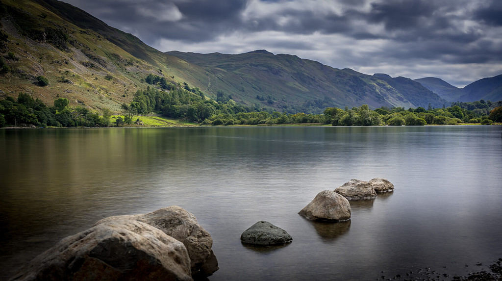 Moody vista che si affaccia su acque calme al lago Ullswater con le montagne in lontananza nel distretto del lago, Cumbria, Regno Unito