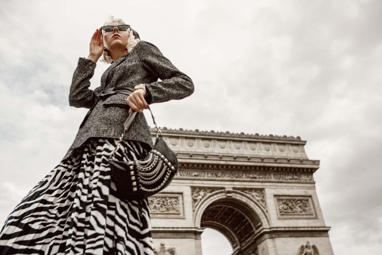 Ritratto di moda autunnale all'aperto di una donna elegante e lussuosa che indossa un blazer bouclé alla moda, una gonna midi a pieghe con stampa zebrata, con in mano una borsa baguette, in posa vicino all'Arco di Trionfo a Parigi.  Copia spazio