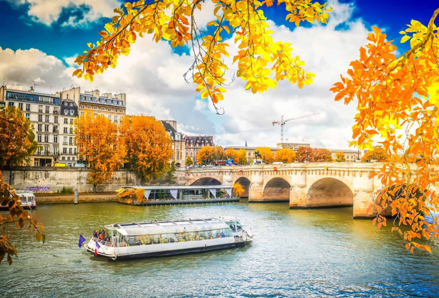Pont Neuf e le acque del fiume Senna con nave da crociera, cielo azzurro con nuvole, Parigi in autunno, Francia con il sole