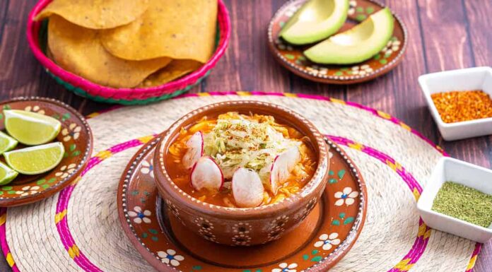 Cibo messicano tradizionale.  Zuppa di pozole rossa con pollo accompagnata da avocado, lattuga, cipolla, ravanello, limone, peperoncino e tortillas di mais croccanti conosciute anche come tostadas su sfondo di legno.