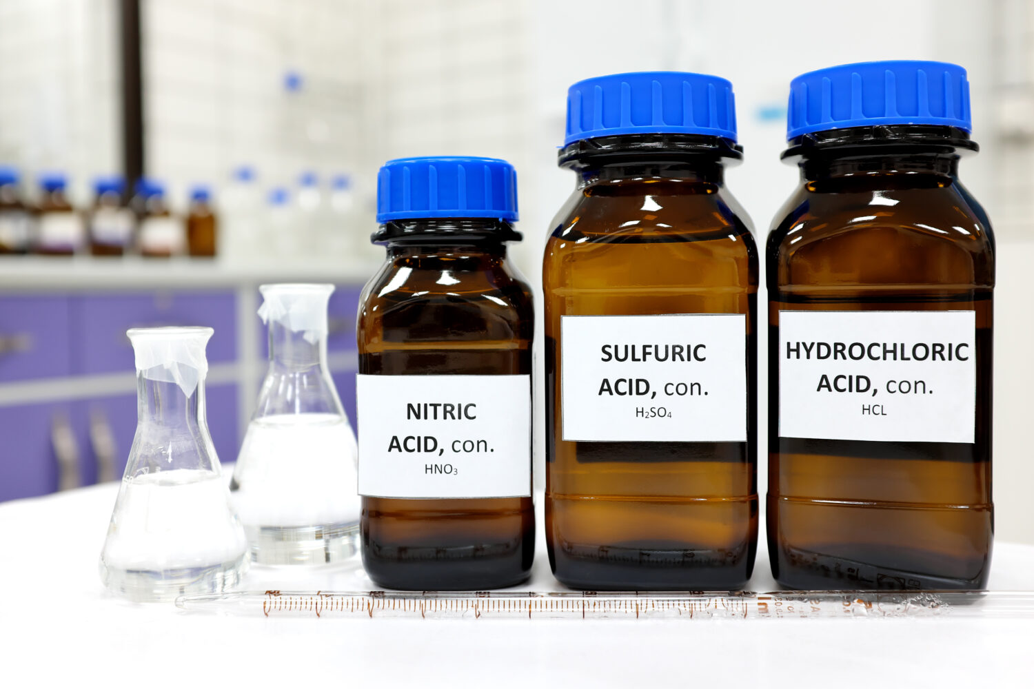 Concentrazione selettiva di forti acidi nitrico, solforico e cloridrico in bottiglia ambrata marrone.  Sfocatura dello sfondo bianco del laboratorio con spazio per la copia.