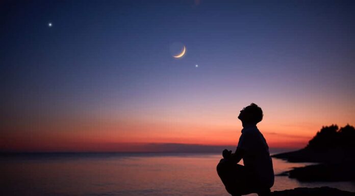 Silhouette di un uomo che guarda la luna e le stelle sull'orizzonte del mare e dell'oceano.