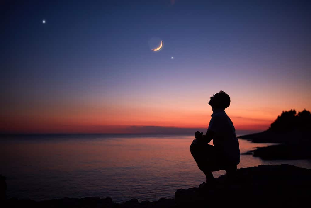 Silhouette di un uomo che guarda la luna e le stelle sull'orizzonte del mare e dell'oceano.