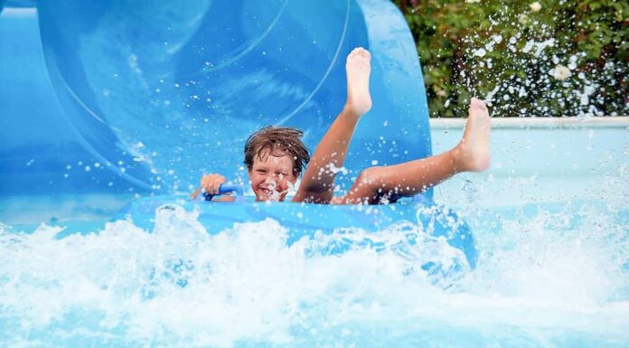 felice che un bambino di 8 anni stia cavalcando nel parco acquatico su cerchi gonfiabili su scivoli d'acqua con spruzzi