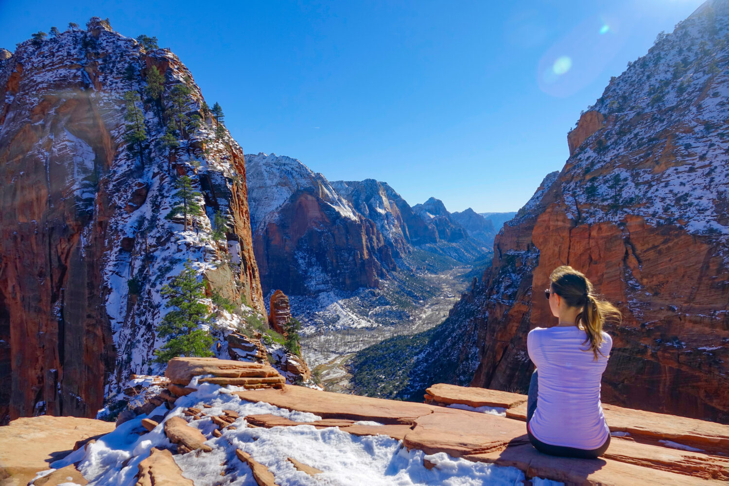 LENTE FLARE: La ragazza viaggiatrice si siede e osserva il canyon innevato da Angel's Landing.  Una giovane donna si siede dopo un'escursione e guarda il bellissimo canyon di colore rosso nel Parco nazionale di Zion, nello Utah.