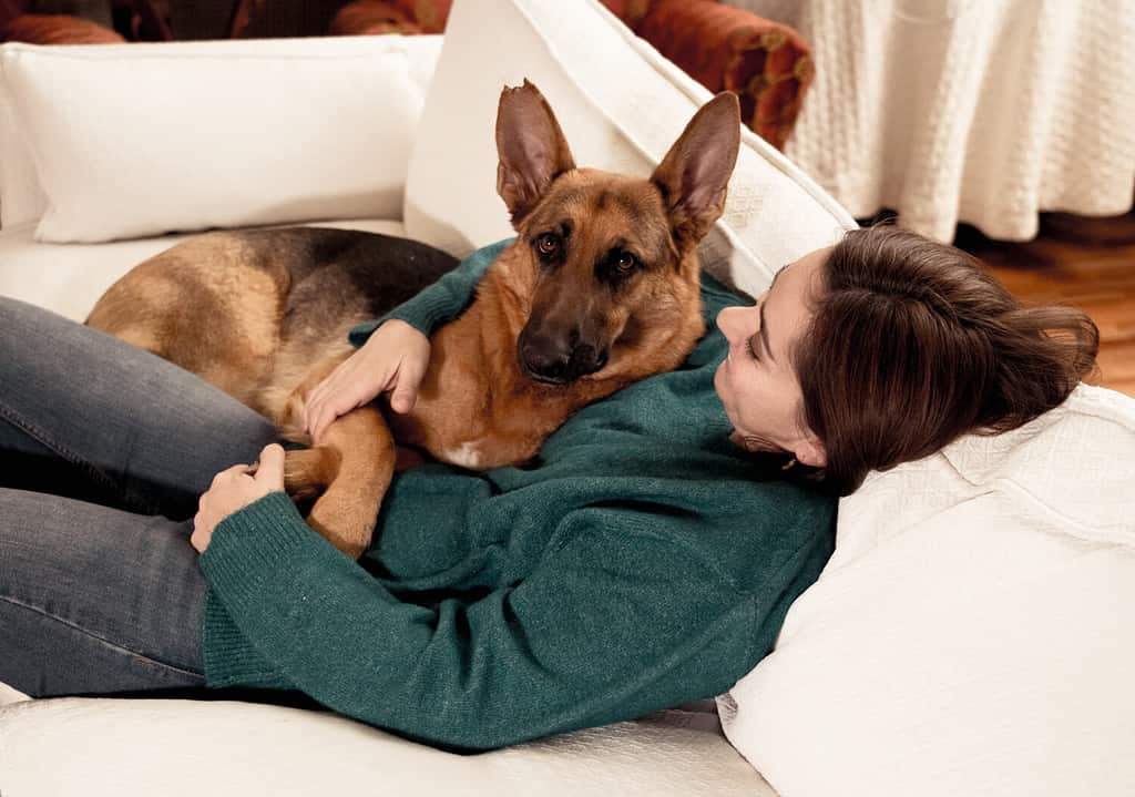 Bellissimo ritratto di donna sorridente che abbraccia il suo cane pastore tedesco insieme davanti al caminetto in casa accogliente in una giornata invernale in allegria Amicizia Amore Compagnia e benefici degli animali domestici.