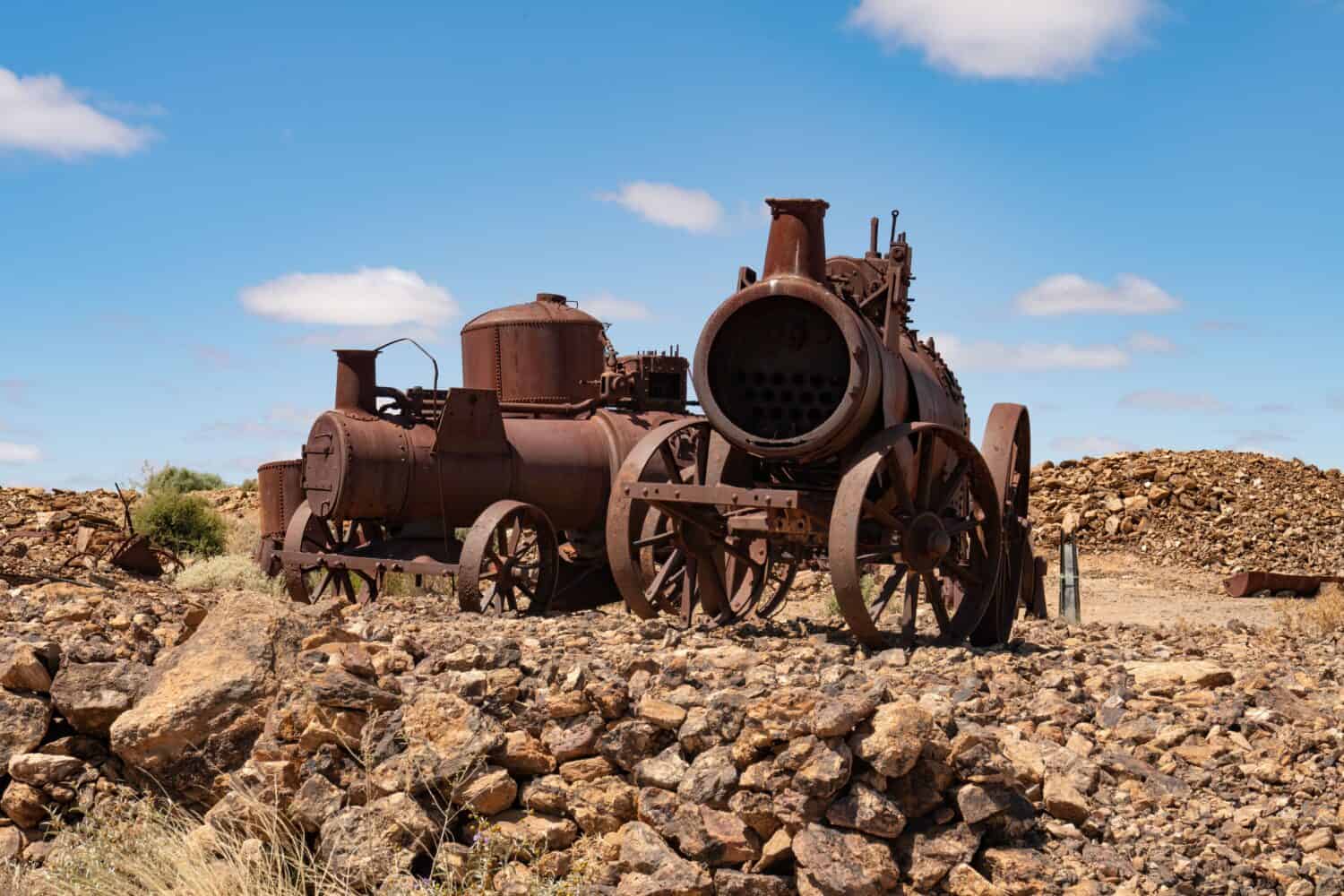 Due vecchi motori a vapore minerari nel deserto a Silverton, Nuovo Galles del Sud, Australia.  Soffici nuvole bianche nel cielo blu.