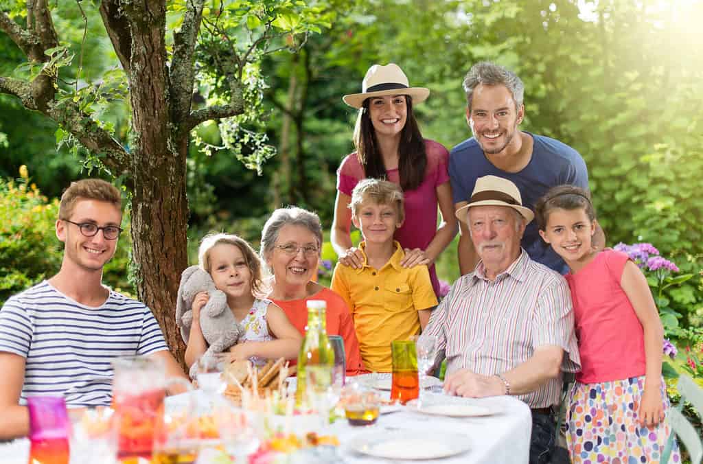 In estate, riunione di famiglia attorno a un tavolo da picnic in uno splendido giardino.  Tutte le generazioni posano per la macchina fotografica.  Girato con bagliore