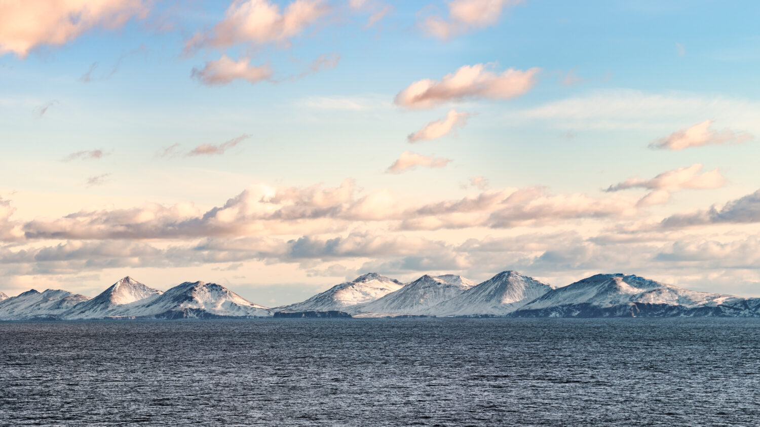 Cime innevate, ghiacciai e rocce delle isole Aleutine nella soleggiata giornata invernale visti dalla nave che passa nel mare calmo