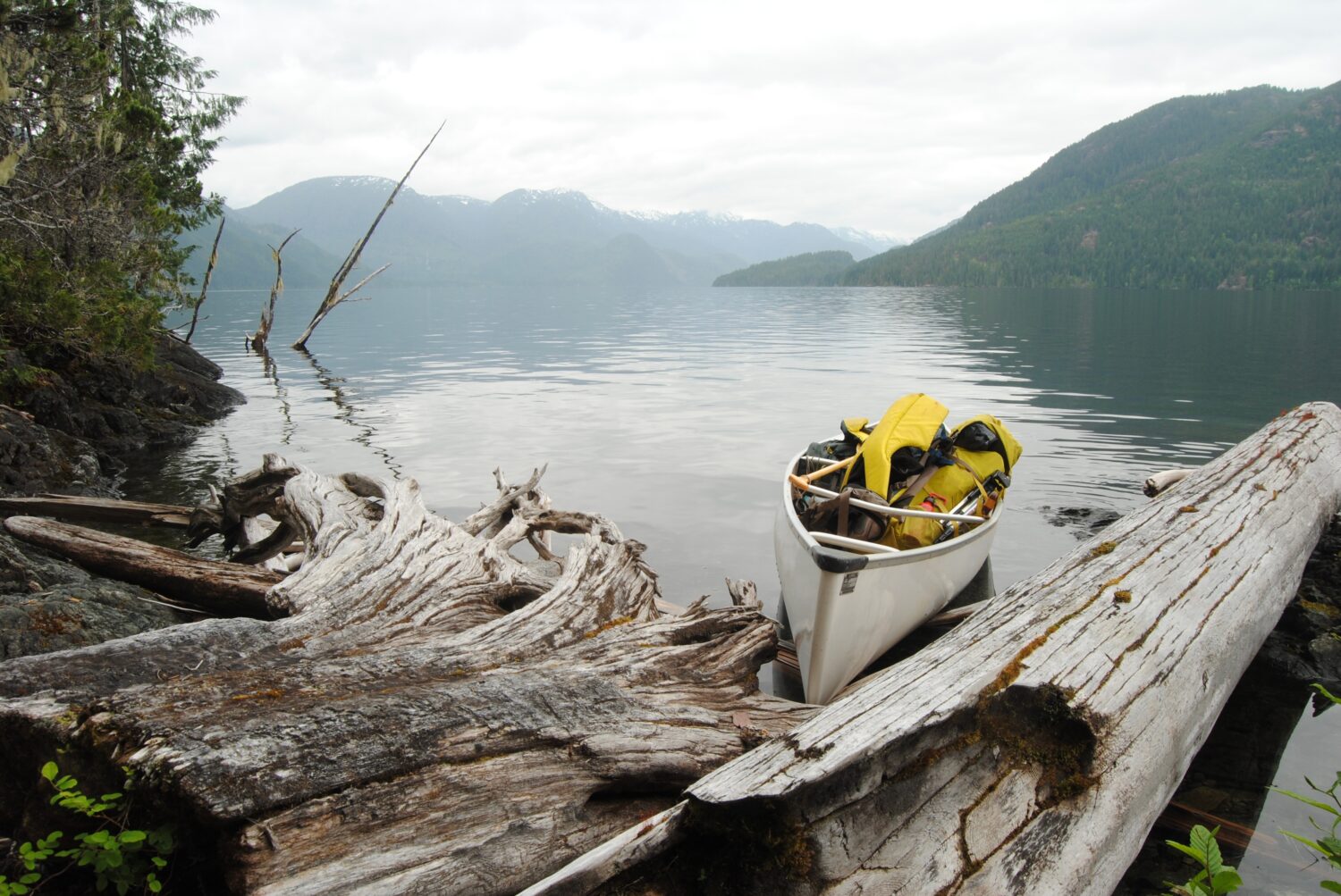 Una canoa da spedizione si trova sulla riva di un tranquillo Grande Lago Centrale, Isola di Vancouver, BC, Canada