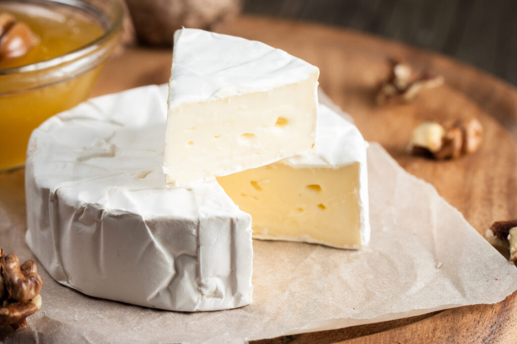 Tipo di formaggio Brie.  Formaggio camembert.  Formaggio Brie fresco e una fetta su una tavola di legno con noci, miele e foglie.  Formaggio italiano, francese.