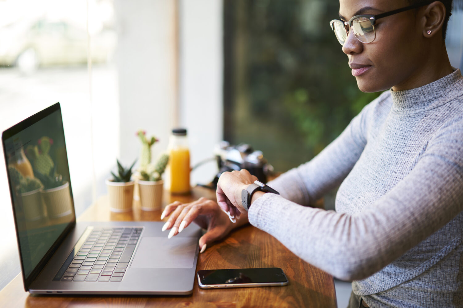 Prospera imprenditrice afroamericana in occhiali alla moda che controlla il tempo mentre aspetta la conferma del pagamento che effettua una transazione online, proprietaria dell'azienda guarda l'orologio in attesa di un incontro 