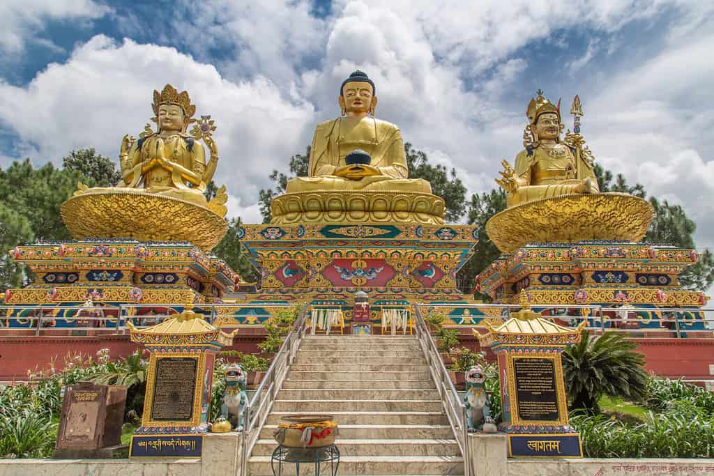 Grandi statue dorate di Avalokiteshvara, Buddha Shakyamuni e Padmasambhava sui troni di loto nel parco di Buddha, area di Swayambhunath, Kathmandu, Nepal