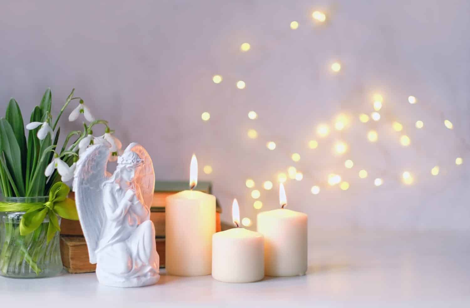 Angelo in preghiera, candele, fiori e libri sul tavolo da vicino, sfondo chiaro astratto.  Concetto di vacanze di Natale o Pasqua.  Festa religiosa in chiesa.  simbolo della fede in Dio, festa del cristianesimo